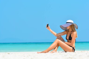 Neşeli genç kadın tropik plaj seyahat Karayip tatilkendini akıllı telefon selfie resimleri çekerek eğleniyor. Mutlu Avrupalı kız model deniz kenarında moda şapka giyiyor. Yaz yaşam tarzı.