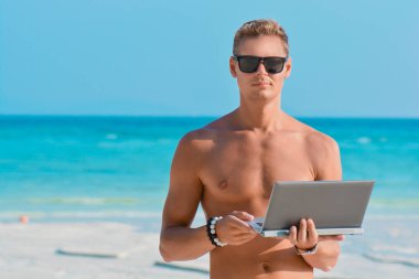 Kumsalda dizüstü bilgisayarıyla çalışan genç adam. Deniz kıyısında defter üzerinde çalışan bir adam. Tropikal plajda tabletli serbest yazar..