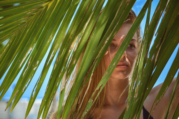 portrait of tender woman looking out of palm leaf. Beautiful woman with shadows of palm leaf on her face.