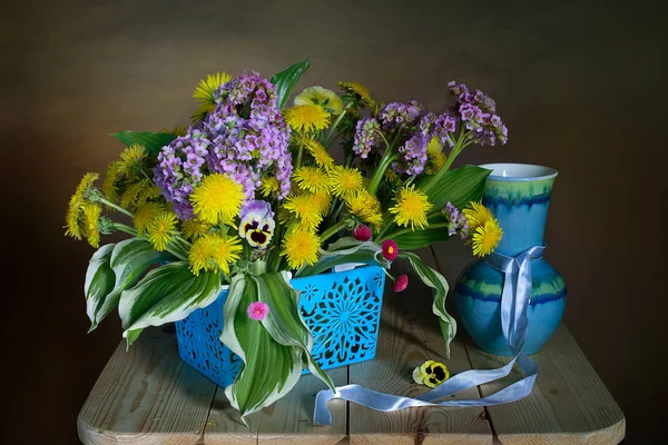 Beautiful bouquet of violets, dandelions and purple flowers in a vase, isolated on a brown background