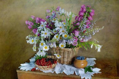 Bir sepet, olgun Frenk üzümü çilek ve yaban mersini masada kır çiçekleri ile natürmort