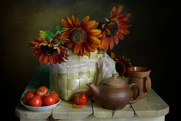 Still life with large sunflowers in a vase and ripe red volumes on a plate on a brown background