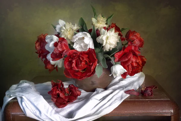 Still life with red poppies, white daffodils in a vase on a table on a green-brown background