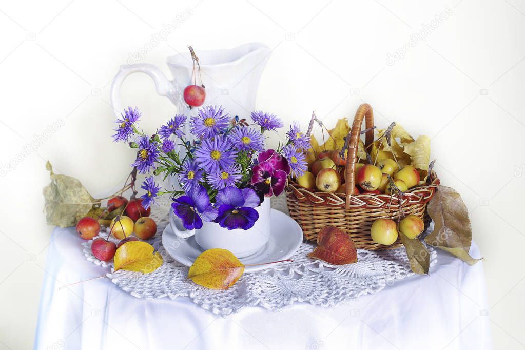 Still life with a bouquet of blue daisies, pansies in a vase, ripe apples in a basket on a white background.