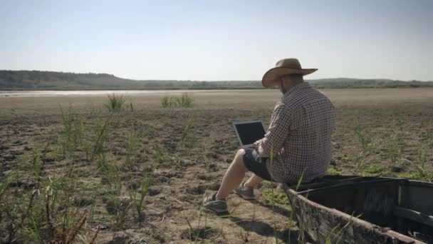Hombre trabajando fuera de la oficina con el ordenador portátil sentado en la orilla del lago — Vídeos de Stock