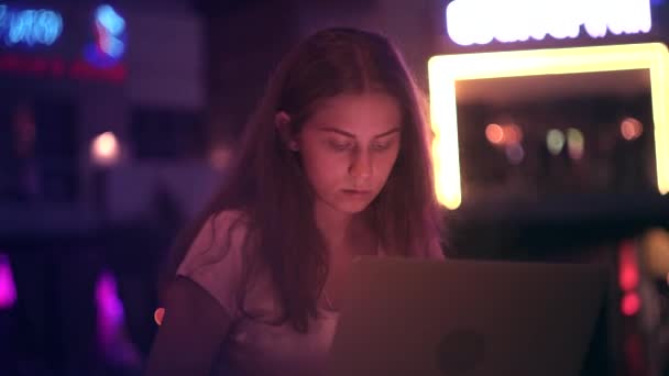 Das Mädchen arbeitet außerhalb des Büros mit einem Laptop in der nächtlichen Stadt — Stockvideo