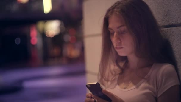 Retrato de una chica con café y un smartphone en una ciudad nocturna — Vídeos de Stock