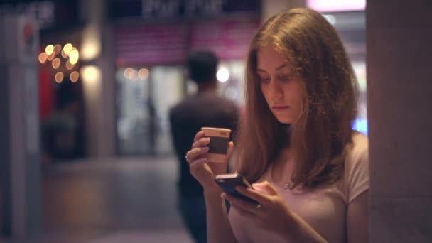 Retrato de una chica con café y un smartphone en una ciudad nocturna — Vídeos de Stock