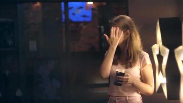 Retrato de una chica con café y un smartphone en una ciudad nocturna — Vídeos de Stock