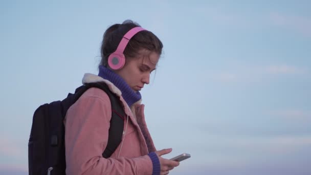 日没時にスマートフォンでビーチに立つ自然な顔を持つ若い女性のクローズアップポートレート — ストック動画