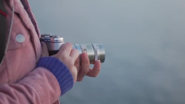 Chica en auriculares toma una foto de la puesta de sol del mar en su cámara vintage — Vídeos de Stock