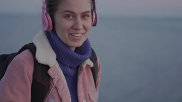 Крупним планом дівчина, посміхаючись, стоїть біля моря, тримаючи вінтажну камеру в руці — стокове відео
