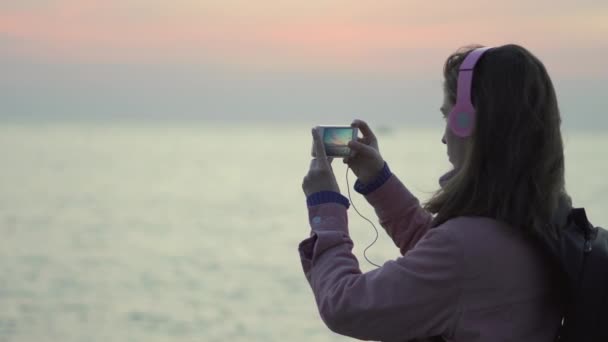 Egy lány fotózni a tenger naplementét használ neki smartphone — Stock videók
