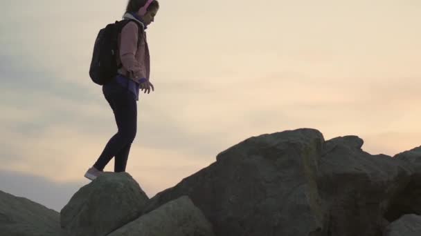 Genç bir gezgin kız tepe boyunca yürüyor. Dik bir dağ, gün batımında okyanus manzarası sunuyor. — Stok video