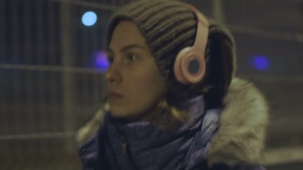 A menina em fones de ouvido sem fio, vai para a cidade da noite — Vídeo de Stock