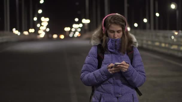 Mujer atractiva usando teléfono móvil durante un paseo por las calles de la ciudad nocturna — Vídeo de stock