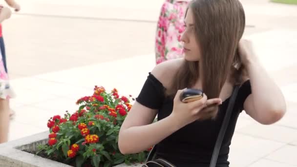 Menina atraente penteando seu cabelo enquanto sentada em um banco em uma rua da cidade — Vídeo de Stock