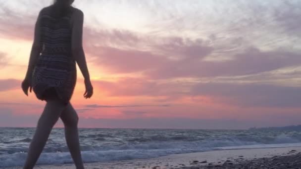 Ein Mädchen in einem Kleid geht bei Sonnenuntergang an der Küste entlang — Stockvideo