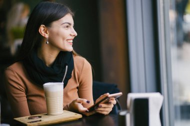 Esmer kız restoranda telefon kullanıyor.