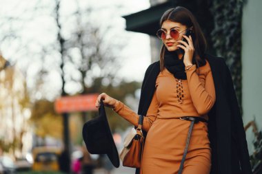 Şık bir kız telefonunu kullanarak şehirde dolaşıyor.