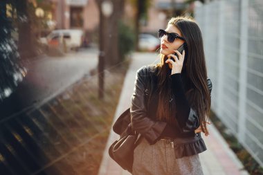 Şık bir kız telefonunu kullanarak şehirde dolaşıyor.