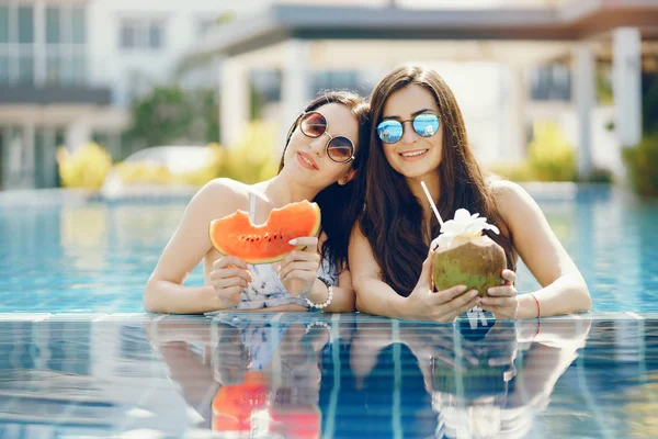 Duas meninas bronzeando e tendo frutas na piscina — Fotografia de Stock