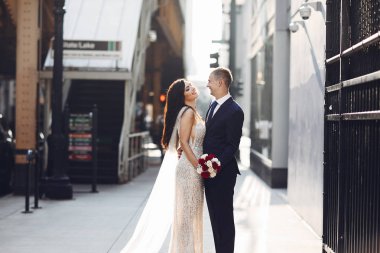 Bir yaz şehrinde yürüyen zarif bir düğün çifti. Mavi takım elbiseli adam. Beyaz, zarif elbiseli bir kadın ve gül buketi.