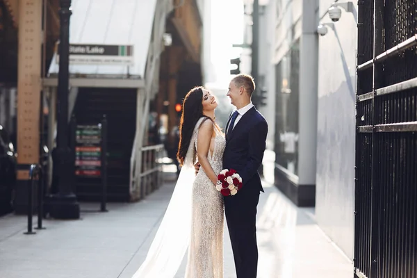 Bir yaz şehrinde yürüyen zarif bir düğün çifti. Mavi takım elbiseli adam. Beyaz, zarif elbiseli bir kadın ve gül buketi.