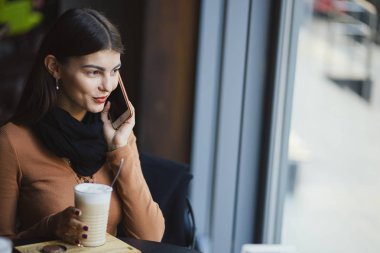 Esmer kız restoranda telefon kullanıyor.