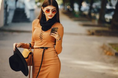 Şık bir kız telefonunu kullanarak şehirde dolaşıyor.