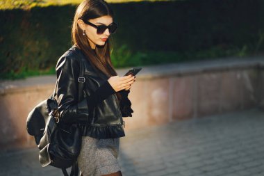 Şık bir kız telefonunu kullanarak şehirde dolaşıyor.