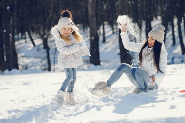 Uzun siyah saçlı, genç ve şık bir anne. Kar parkında küçük tatlı kızıyla oynuyor.