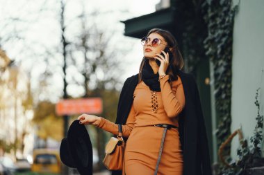 Şık bir kız telefonunu kullanarak şehirde dolaşıyor.