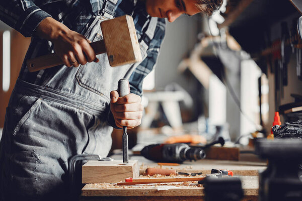 A man carves a tree. The carpenter works with a hammer in a studio. An engineer provides a tree shape