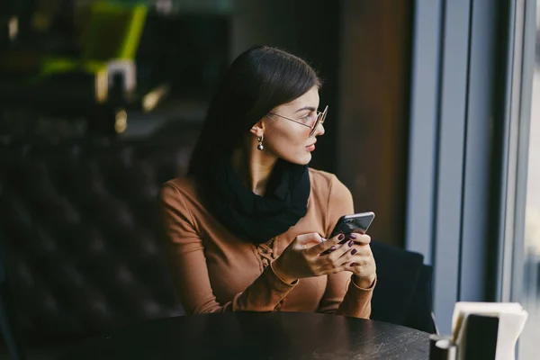 Brunette girl using phone while at a restaurant — Stock Photo, Image