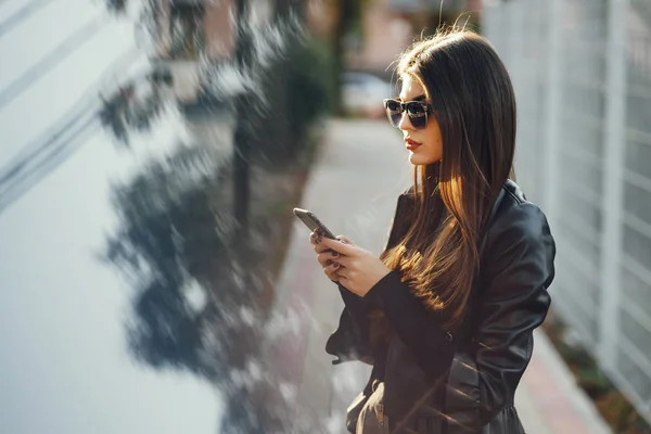 Chica elegante caminando por la ciudad mientras usa su teléfono — Foto de Stock