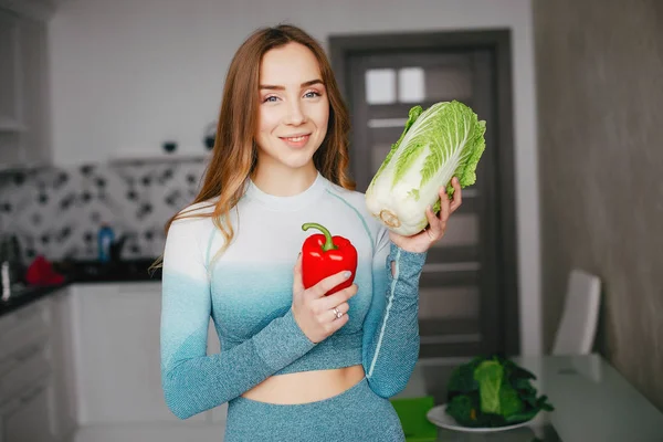 Sport flicka i ett kök med grönsaker — Stockfoto