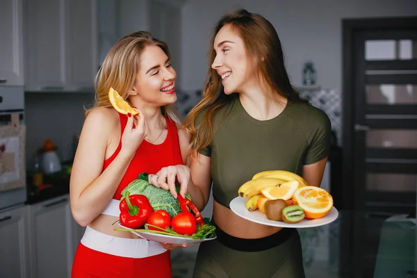 Twee sporten meisje in een keuken met groenten — Stockfoto