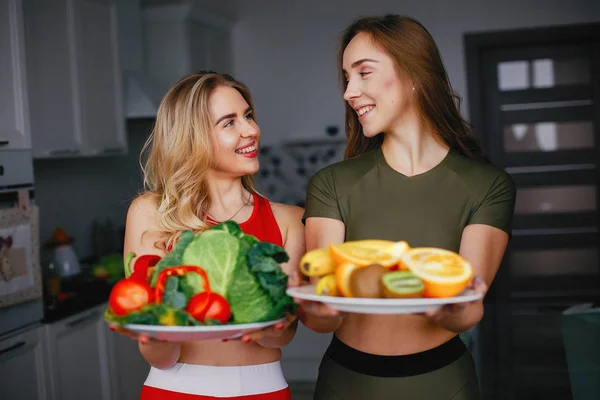 Dois esportes menina em uma cozinha com legumes — Fotografia de Stock
