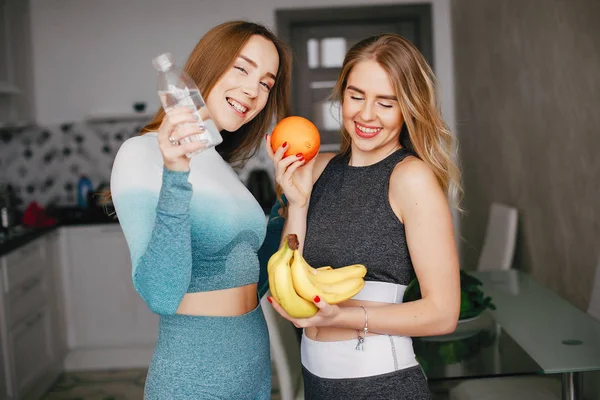 Two sports girl in a kitchen with vegetables