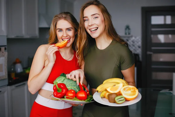 Två sporter flicka i ett kök med grönsaker — Stockfoto