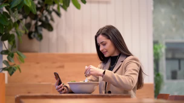 Видео, где девушка ест салат и пользуется мобильным телефоном — стоковое видео