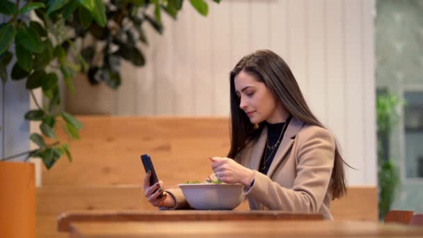 Videó a lány eszik egy salátát, és használja a mobiltelefonján — Stock videók