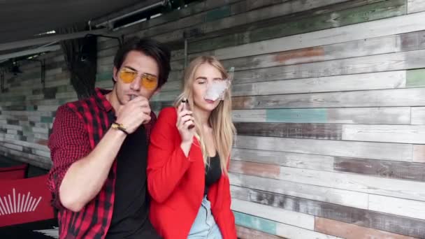 Pareja con estilo en una ciudad. Dos personas usan el cigarrillo electrónico — Vídeos de Stock