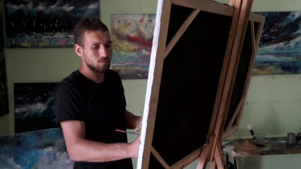 Художник-мужчина рисует картину в студии — стоковое видео