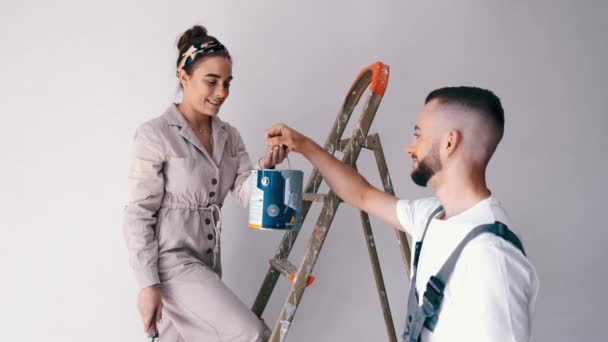 Hustru stående på en stege medan hennes man målar väggen — Stockvideo