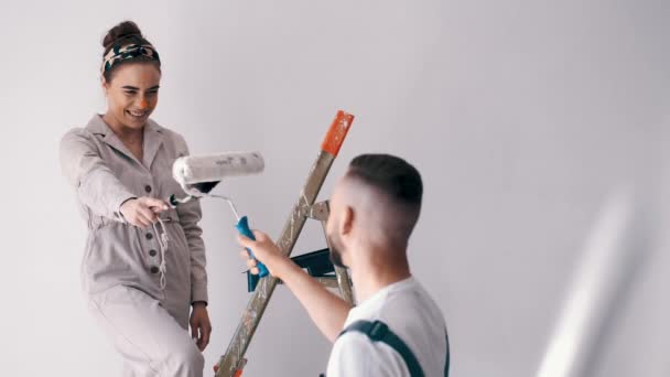 Wife standing on a ladder while her husband paints the wall — Stock Video