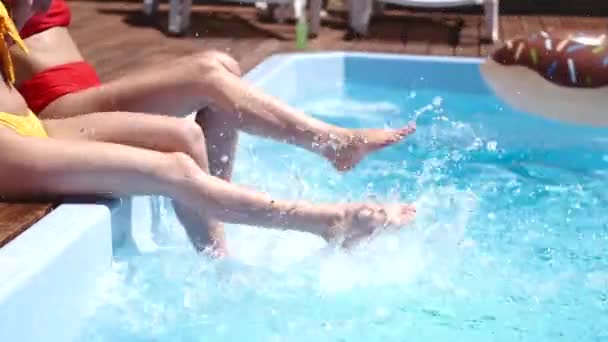 Dos chicas salpicando sus piernas en la piscina — Vídeos de Stock