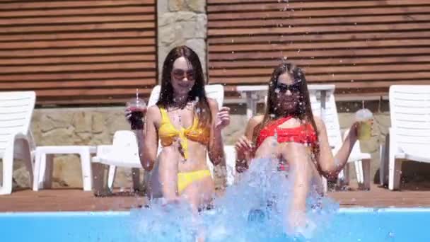 Dos chicas salpicando sus piernas en la piscina — Vídeo de stock