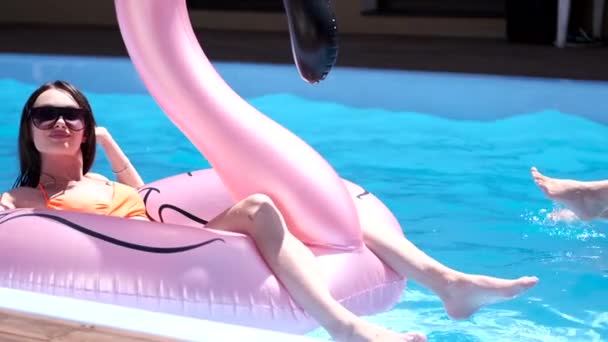 Dos chicas felices en traje de baño colorido con hermosas figuras se están divirtiendo en juguetes inflables en la piscina — Vídeos de Stock